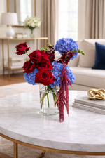 Decorative floral arrangement in a glass vase on a marble coffee table with a living room background.