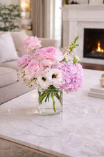 Bouquet of pink and white flowers in a clear vase on a marble coffee table with a fireplace in the background.