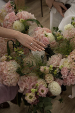 Person wearing a ring touching a bouquet of flowers with another person partially visible.